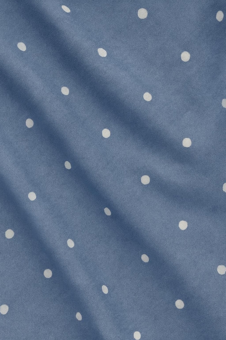 May include: Close-up of a blue fabric with a pattern of evenly spaced white polka dots. The fabric is slightly wrinkled, creating shadows and variations in the blue color. The polka dots are round and consistent in size.