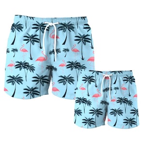 Puede incluir: Un par de pantalones de baño azules con un estampado de flamencos y palmeras. Los pantalones tienen una cintura con cordón y están disponibles en dos tallas.