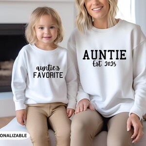May include: Two white sweatshirts with black text. One sweatshirt says "Auntie Est. 2025" and the other says "auntie's FAVORITE".