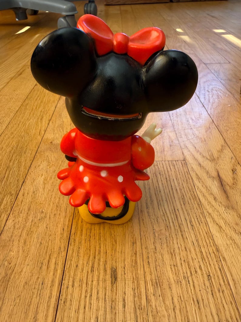 Op de afbeelding: Een Minnie Mouse-beeldje, met een zwarte kop, grote oren en een rode strik. Het beeldje draagt een rode jurk met witte stippen en een gele basis. Dit is een verzamelobject.