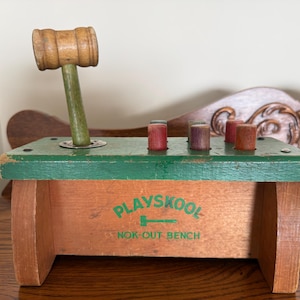 May include: A vintage Playskool Nok-Out Bench toy. The wooden bench has a green top with five coloured pegs and a wooden mallet. The bench is brown with the words "Playskool Nok-Out Bench" printed in green.