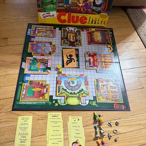 May include: The Simpsons Clue board game, featuring a green game board with room illustrations, character cards, dice, and game pieces. The box art shows the Simpsons family. The game includes character figurines and weapon tokens.