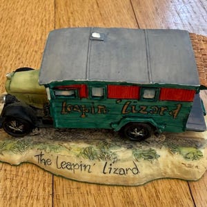 Puede incluir: Figura decorativa de una caravana verde y roja con el texto "Leapin' Lizard" en el lateral. La caravana tiene un techo gris y se asienta sobre una base con las palabras "The Leapin' Lizard".