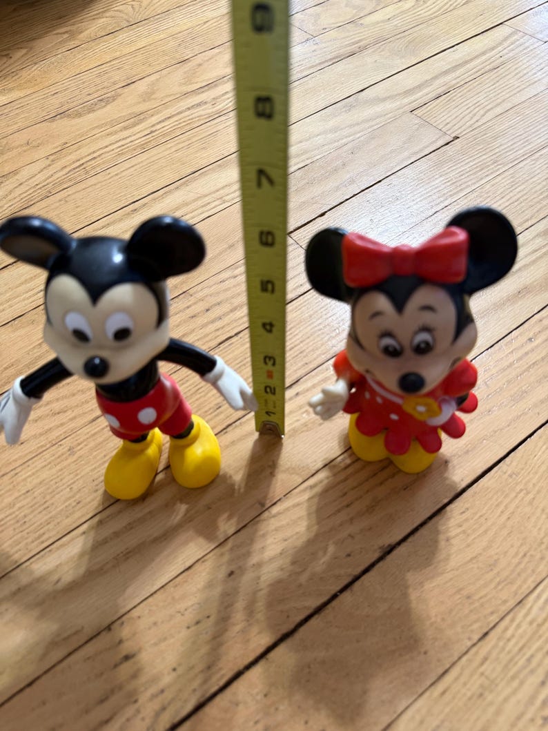 Op de afbeelding: Twee Disney-beeldjes van Mickey Mouse en Minnie Mouse worden getoond. Mickey draagt een rode broek, gele schoenen en witte handschoenen. Minnie draagt een rode jurk met een rode strik. De figuren zijn ongeveer 7.6 cm hoog.