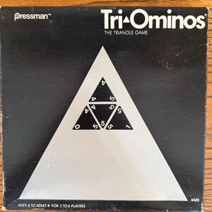 May include: A square black board game box for Tri-Ominos, The Triangle Game by Pressman. The cover features a large white triangle containing smaller black triangular tiles with white numbers. Text includes Ages 8 to Adult, 2 to 6 players, and 4420.