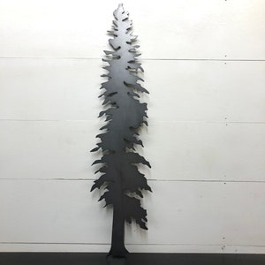 May include: A black metal tree silhouette against a white wooden background. The tree has a detailed, textured design with branches and a trunk. The artwork is a decorative piece, suitable for indoor or outdoor display.