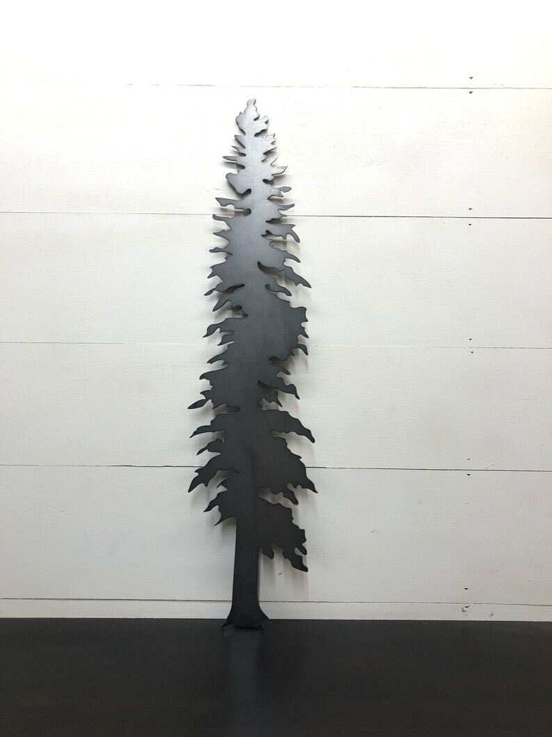 May include: A black metal tree silhouette against a white wooden background. The tree has a detailed, textured design with branches and a trunk. The artwork is a decorative piece, suitable for indoor or outdoor display.