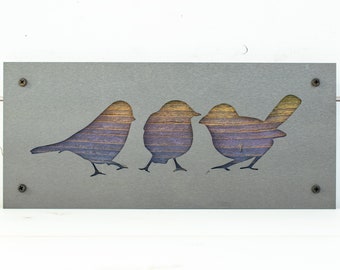 May include: A gray metal wall decor with three cutout silhouettes of birds. The birds are in a row and are facing the right. The birds are a light brown color with a gradient of purple and blue.