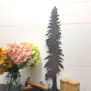 May include: A dark metal tree silhouette stands tall against a white wood-paneled wall. A bouquet of pink and yellow flowers in a glass jar, two wooden spools, and two small, floral-decorated boxes complete the rustic decor.