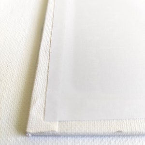 May include: Close-up of the edge of a white canvas, showing the raw canvas texture and the smooth, white surface of the stretched canvas.
