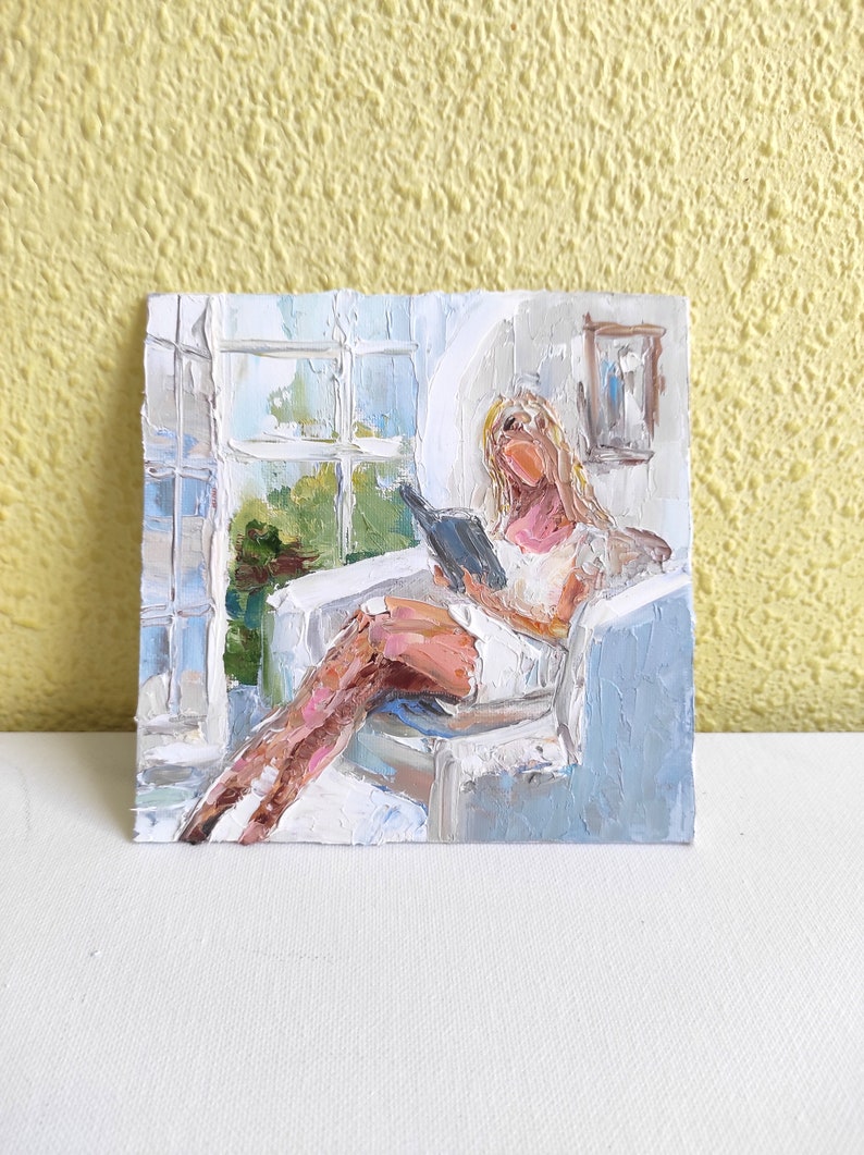 May include: A painting of a person sitting in a chair by a window, reading a book. The person is wearing a white dress and has blonde hair. The painting is done in a loose, impressionistic style.