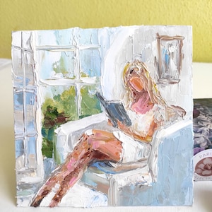 May include: A painting of a person sitting in a chair by a window, reading a book. The person has blonde hair and is wearing a white dress. The painting is done in a loose, impressionistic style with thick brushstrokes.