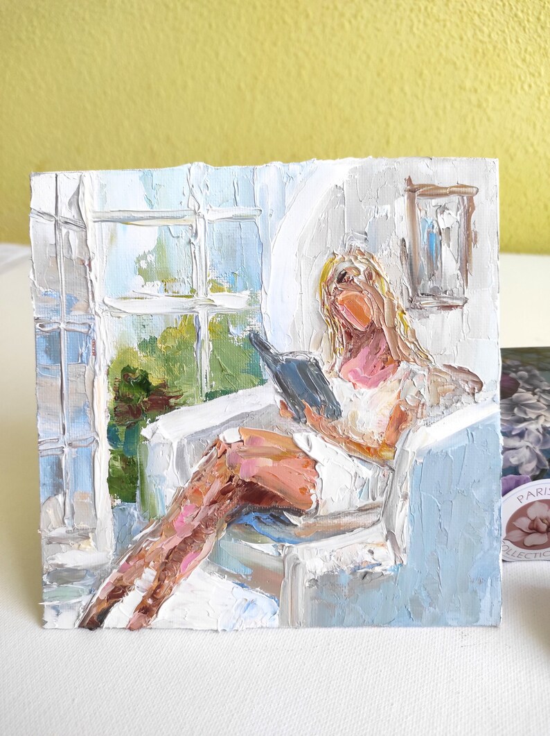 May include: A painting of a person sitting in a chair by a window, reading a book. The person has blonde hair and is wearing a white dress. The painting is done in a loose, impressionistic style with thick brushstrokes.