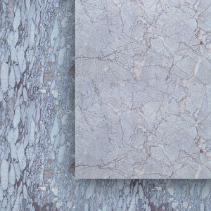 May include: A close-up of two marble slabs. The slab on the right is a light gray with subtle brown veining. The slab on the left is a darker gray with more pronounced brown and white veining, creating a textured appearance.