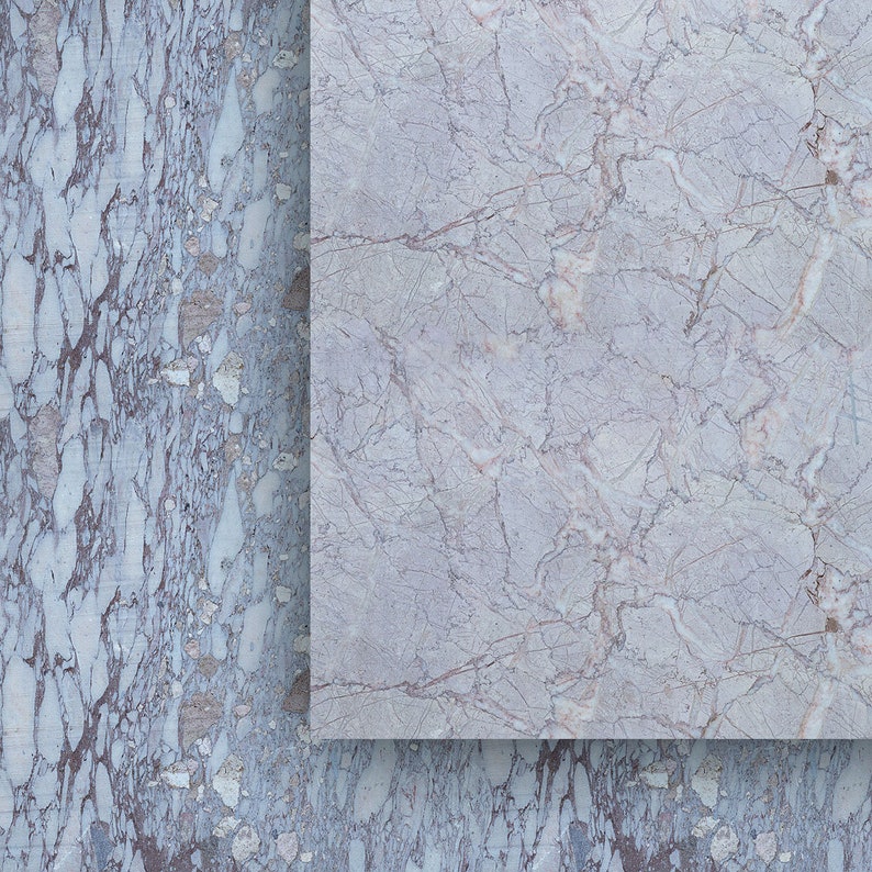 May include: A close-up of two marble slabs. The slab on the right is a light gray with subtle brown veining. The slab on the left is a darker gray with more pronounced brown and white veining, creating a textured appearance.