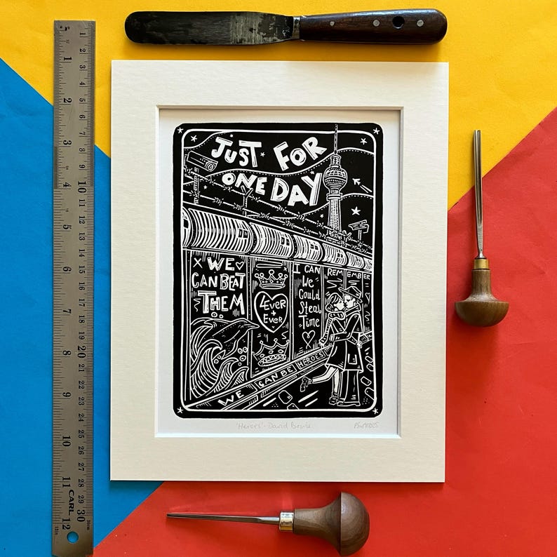 May include: Black and white linocut print of a couple walking down a street in Berlin, Germany. The print features the text "Just for one day" and "We can beat them".