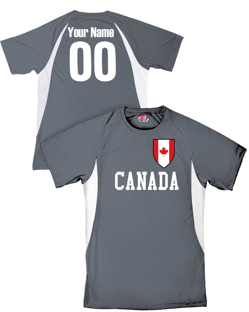 May include: Gray athletic jersey with white accents and the word "CANADA" in white block letters. A shield with a red maple leaf is above the word. The back of the jersey has the text "Your Name" and the number "00".