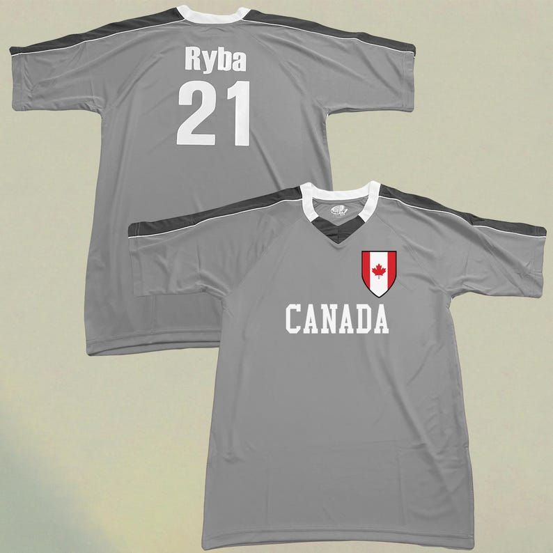 May include: Two grey athletic jerseys. One jersey has the name "Ryba" and the number "21" in white. The other jersey has the word "CANADA" in white, and a red and white Canadian flag emblem.