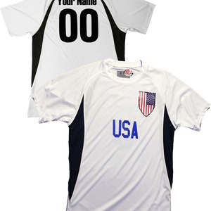 May include: White soccer jersey with black accents and a blue "USA" inscription. The jersey has a black and white American flag patch on the chest. The back of the jersey has a black "00" and the text "Your Name" printed on it.