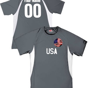 May include: Gray soccer jersey with white accents and a soccer ball with an American flag design on the front. The back of the jersey has the text "Your Name" and the number "00" in white.