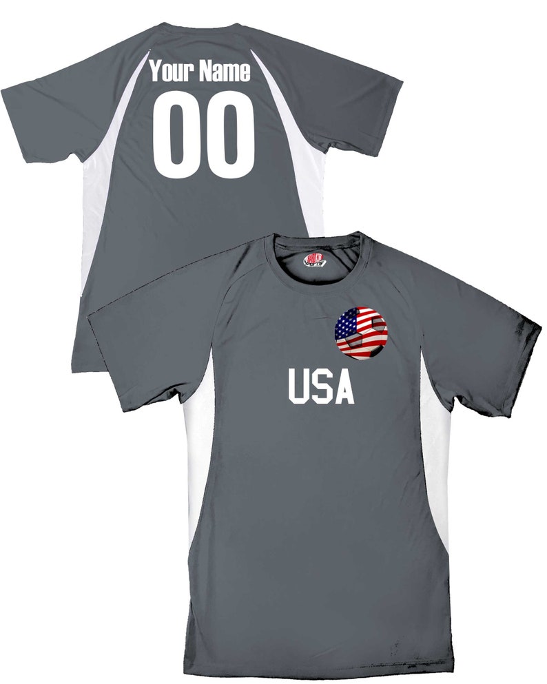 May include: Gray soccer jersey with white accents and a soccer ball with an American flag design on the front. The back of the jersey has the text "Your Name" and the number "00" in white.