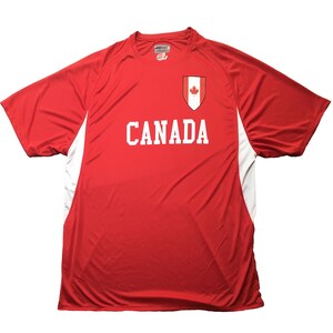 May include: Red athletic t-shirt with white accents and the word "CANADA" in bold white letters. Features a Canadian flag emblem on the chest. The shirt has a crew neck and short sleeves.