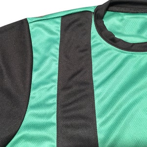May include: Close-up of a green and black athletic jersey. The jersey features a black shoulder and a vertical black stripe down the front. The rest of the jersey is green with a textured pattern.