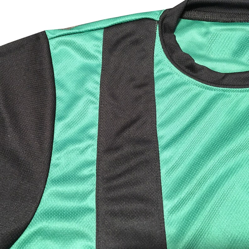 May include: Close-up of a green and black athletic jersey. The jersey features a black shoulder and a vertical black stripe down the front. The rest of the jersey is green with a textured pattern.