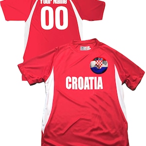 Puede incluir: Camiseta de f&uacute;tbol roja con detalles blancos y un bal&oacute;n de f&uacute;tbol con la bandera croata en la parte delantera. La camiseta tiene la palabra "CROATIA" impresa en la parte delantera y el n&uacute;mero "00" en la parte posterior.