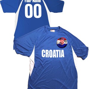 Puede incluir: Una camiseta de f&uacute;tbol azul con detalles blancos y el texto "CROATIA" en la parte delantera. La camiseta presenta un bal&oacute;n de f&uacute;tbol con la bandera croata en &eacute;l. La parte posterior de la camiseta tiene el texto "Your Name" y el n&uacute;mero "00" en blanco.