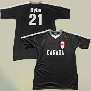 May include: Black football jersey with white shoulder and sleeve detailing. The jersey displays the word "CANADA" in white, a Canadian flag crest, and the name "Ryba" and number "21" on the back.