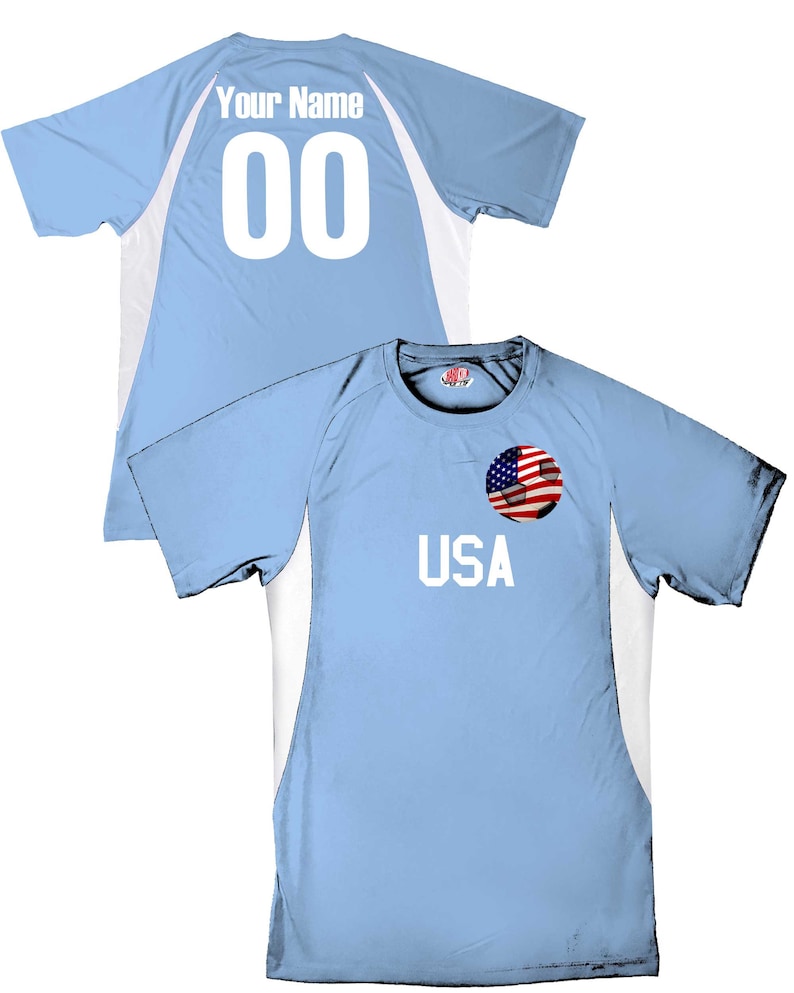May include: Light blue soccer jersey with white accents. The back of the jersey has the text "Your Name" and the number "00". The front of the jersey has the text "USA" and a soccer ball with an American flag.