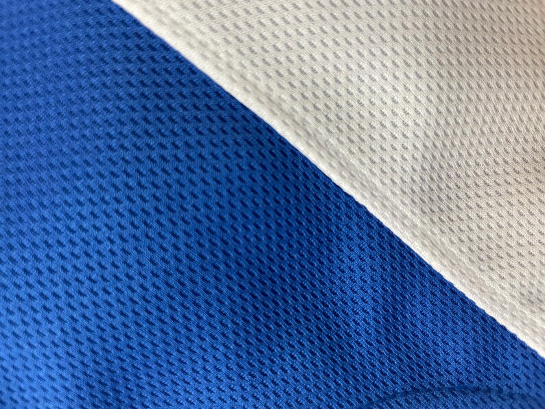 May include: Close-up of a blue and white athletic fabric. The blue fabric is a vibrant royal blue, and the white fabric is a crisp, clean white. Both fabrics have a textured, breathable weave, suggesting a performance material.