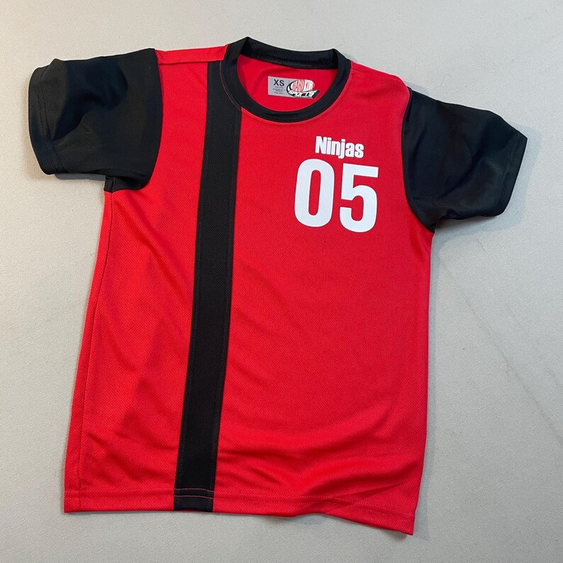 May include: Red and black athletic shirt with the word "Ninjas" and the number "05" in white. The shirt has black sleeves and a black vertical stripe down the left side. The shirt is a size XS.
