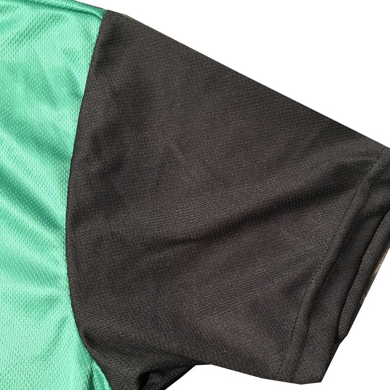 May include: Close-up of a short sleeve athletic shirt. The shirt features a black sleeve and a green mesh fabric on the side. The fabric has a textured appearance. The shirt is likely made of a breathable material.