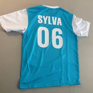May include: A turquoise and white athletic jersey. The back of the jersey features the name "SYLVA" above the number "06" in white block letters. The sleeves are white.
