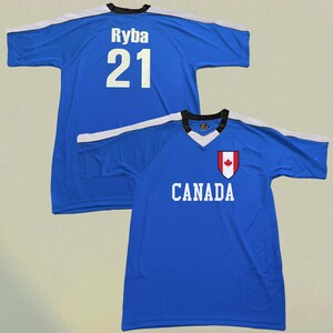 May include: Two blue athletic jerseys. One jersey has the name "Ryba" and the number "21" in white on the back. The other jersey has the word "CANADA" in white and a Canadian flag emblem on the front.