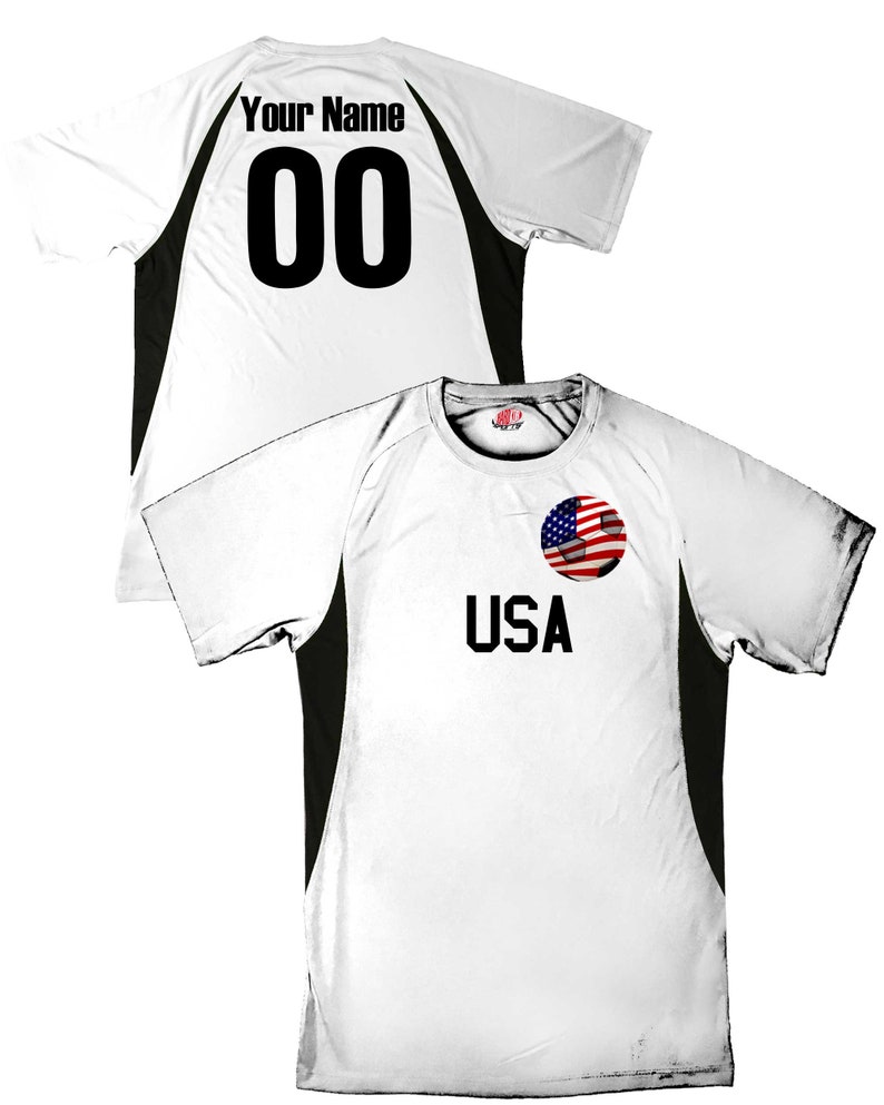 May include: White soccer jersey with black side panels. The back of the jersey has "Your Name" and "00" printed on it. The front of the jersey has "USA" printed on it with a soccer ball with an American flag design.