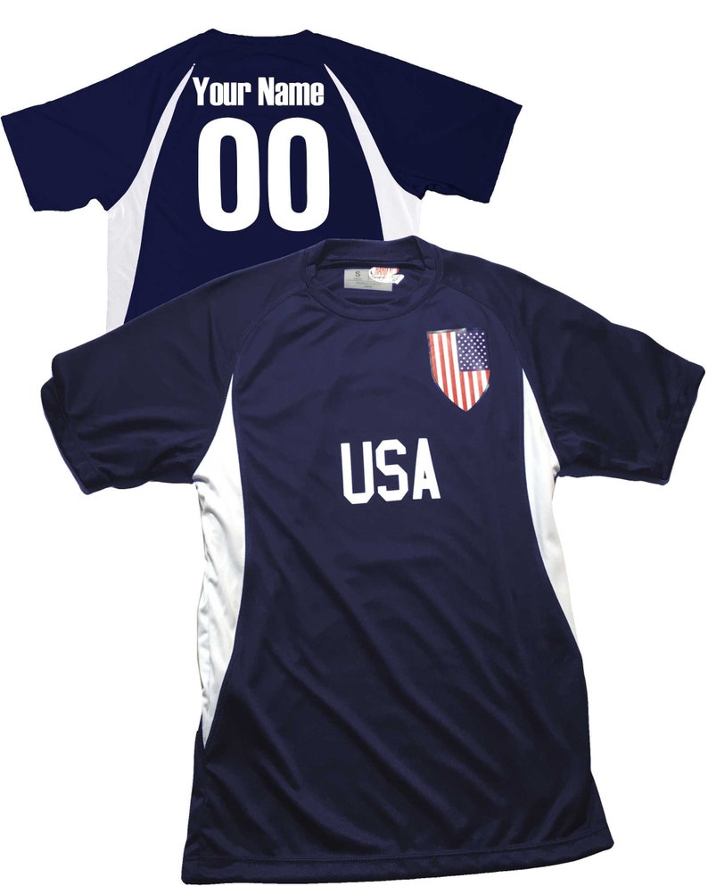 May include: A navy blue soccer jersey with white accents and the word "USA" printed on the front. The jersey has a small American flag patch on the right shoulder. The back of the jersey has a white number "00" and the words "Your Name" printed on it.