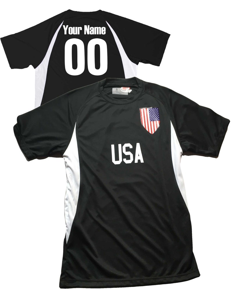 May include: Black soccer jersey with white accents and the word "USA" printed on the front. The back of the jersey has a white number "00" and the text "Your Name".