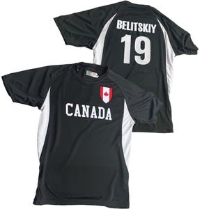 May include: Black athletic shirt with white accents and the word "CANADA" in white block letters. A red maple leaf emblem is above the word. The back of the shirt displays the name "BELITSKIY" and the number "19" in white.