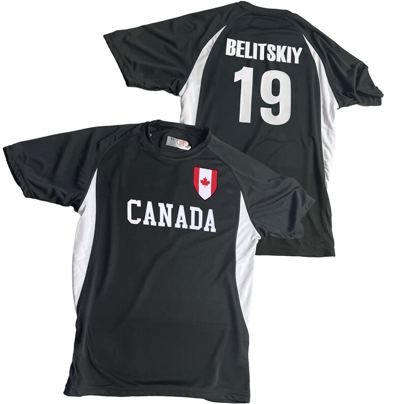 May include: Black athletic shirt with white accents and the word "CANADA" in white block letters. A red maple leaf emblem is above the word. The back of the shirt displays the name "BELITSKIY" and the number "19" in white.