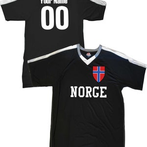 May include: Black soccer jersey with white accents and the word "NORGE" printed on the front. The jersey also features the Norwegian flag on the chest. The back of the jersey has a white number "00" and the text "Your Name" printed on it.