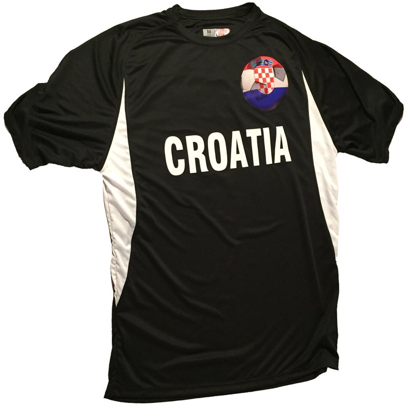Puede incluir: Camiseta de f&uacute;tbol negra con detalles blancos y la palabra "CROACIA" impresa en la parte delantera. Un bal&oacute;n de f&uacute;tbol con la bandera croata est&aacute; impreso en el pecho izquierdo.