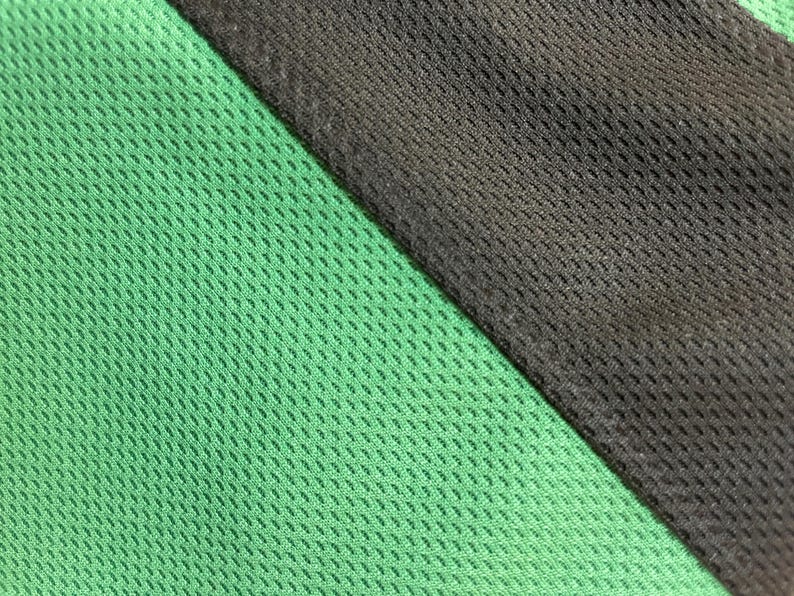 May include: Close-up of a green and black mesh fabric. The green fabric is on the left, and the black fabric is on the right, separated by a diagonal seam. The mesh has a small, evenly spaced pattern.