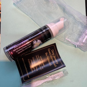 May include: A white bottle of jewelry cleaner with a black label that says "Watchpita" and "Dirty Jewelry Goes Unnoticed. Be Noticed."  The bottle is next to a white cleaning brush and a white mesh bag.