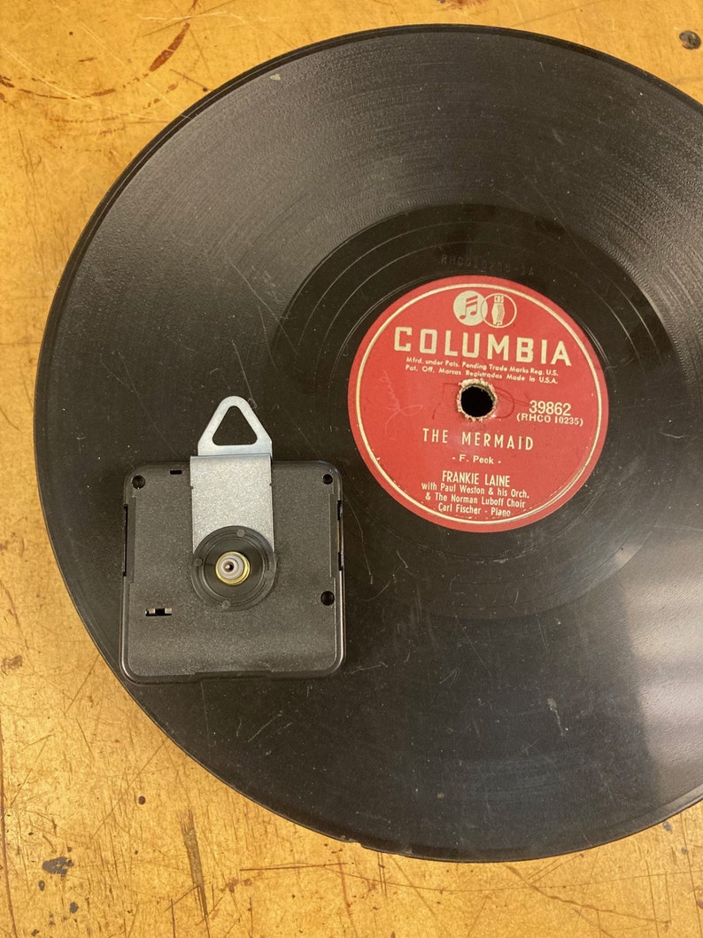 May include: A black vinyl record with a red label. The label has the text "Columbia" in white letters and the text "The Mermaid" in white letters. The record is 39862 (RHCO 10235) and features Frankie Laine with Paul Weston & his Orch. & The Norman Lubeff Choir. Carl Fischer - Piano.