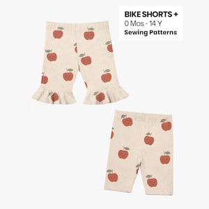 Könnte beinhalten: Zwei Paar Kinder-Fahrradshorts. Ein Paar ist cremefarben mit einem roten Apfelmuster und Rüschensaum. Das andere Paar ist cremefarben mit einem roten Apfelmuster. Der Text "BIKE SHORTS + 0 Mos - 14 Y Sewing Patterns" befindet sich oben rechts.
