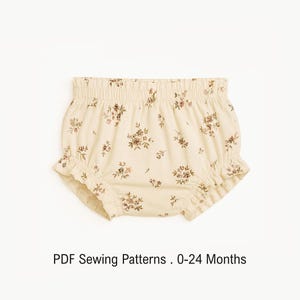 Puede incluir: Bombachos para bebé de color crema con un delicado estampado floral marrón, cintura elástica y aberturas de pierna con volantes. El texto debajo de la prenda dice: PDF Sewing Patterns . 0-24 Months. Diseño con fruncidos.