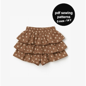 May include: Brown tiered shorts with a white floral pattern. The shorts have an elastic waistband and are made of a soft fabric. The image also includes a black circle with the text "pdf sewing patterns 0 mos - 14 Y".